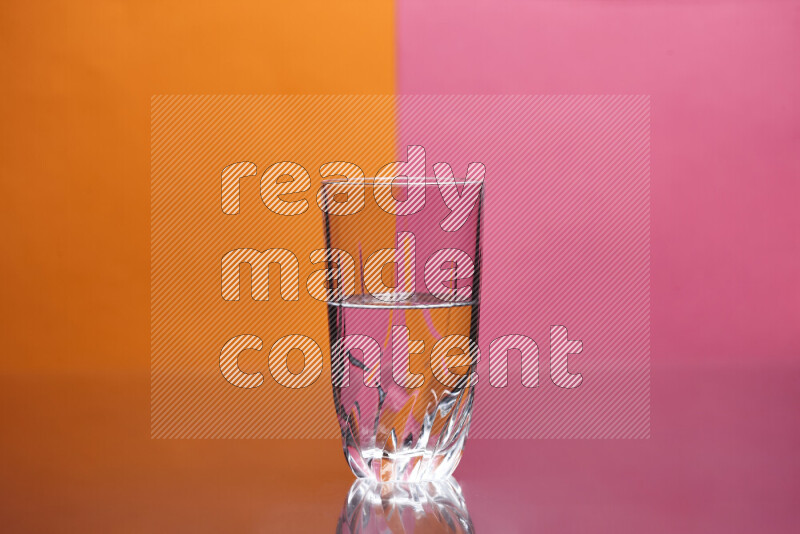 The image features a clear glassware filled with water, set against orange and pink background