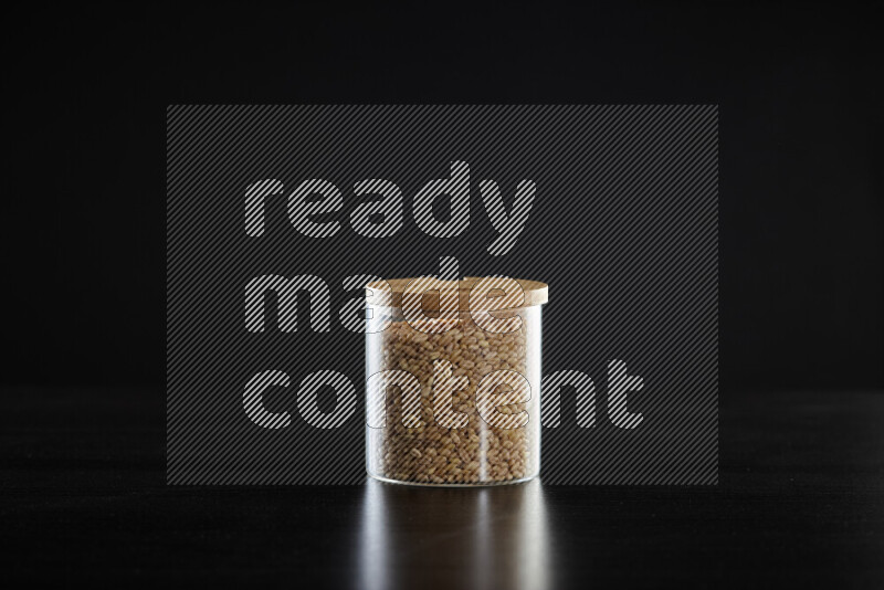 Hulled wheat in a glass jar on black background