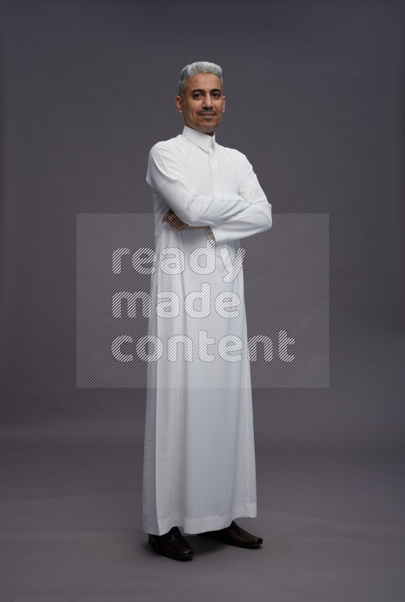 Saudi man wearing thob standing with crossed arms on gray background