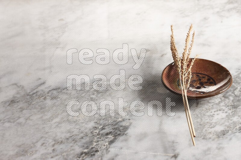 Wheat stalks on decorative pottery plate on grey marble background