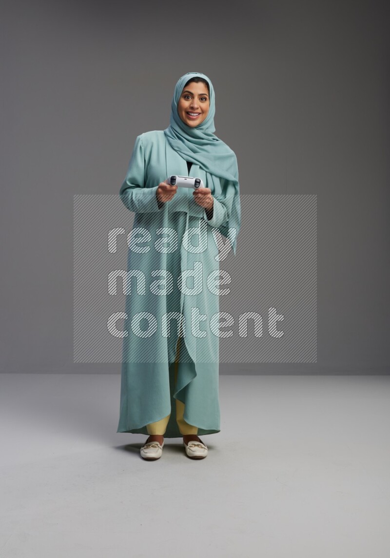 Saudi Woman wearing Abaya standing Playing Games on Gray background