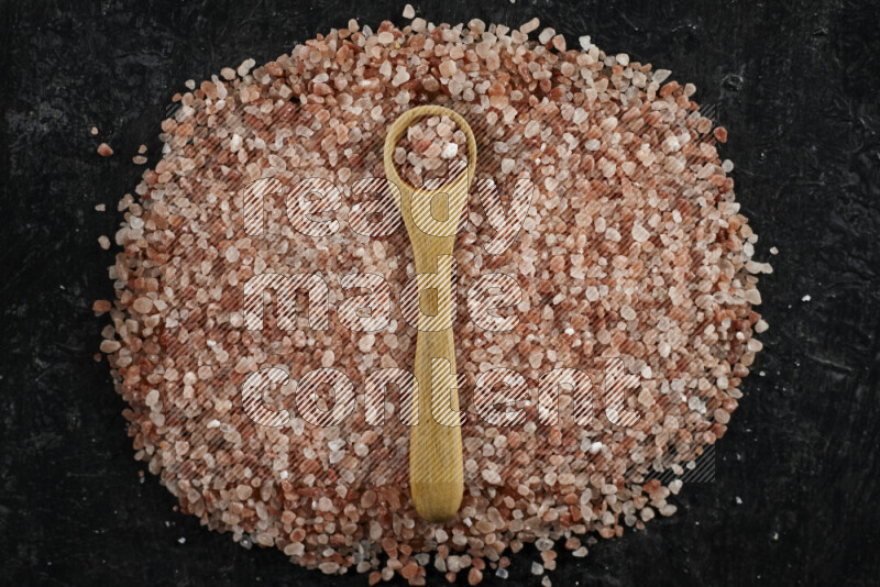 A wooden spoon full of coarse himalayan salt crystals on a bunch of the crystals on black background