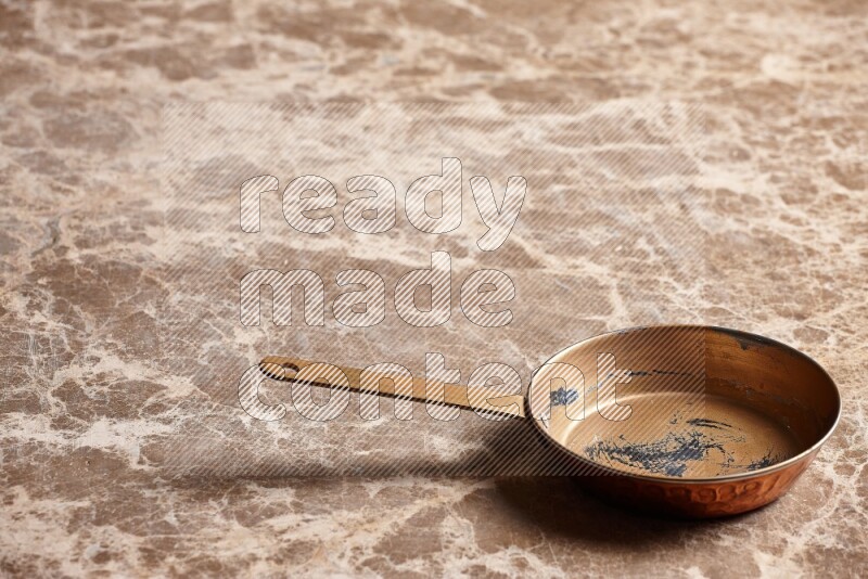 A small copper pan on beige marble background