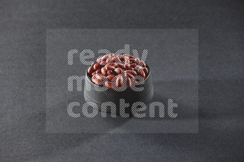 A black pottery bowl full of red skin peanuts on a black background in different angles
