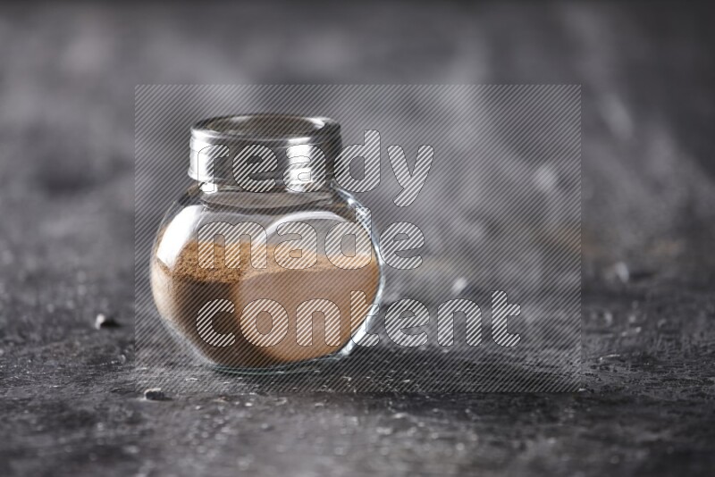 Herbal glass jar full of cinnamon powder on a textured black background