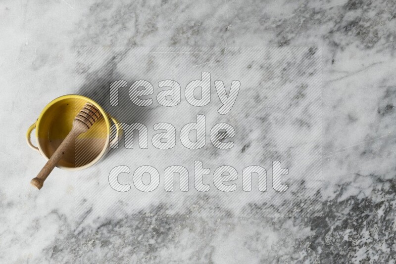 وعاء فخاري متعدد الألوان مع ملعقة عسل خشبية بداخله على خلفية من الرخام الرمادي