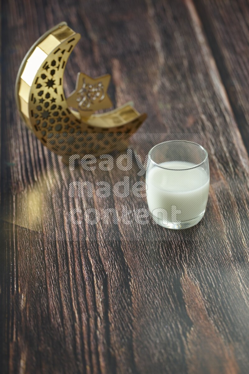 A wooden golden crescent lantern with different drinks, dates, nuts, prayer beads and quran on brown wooden background