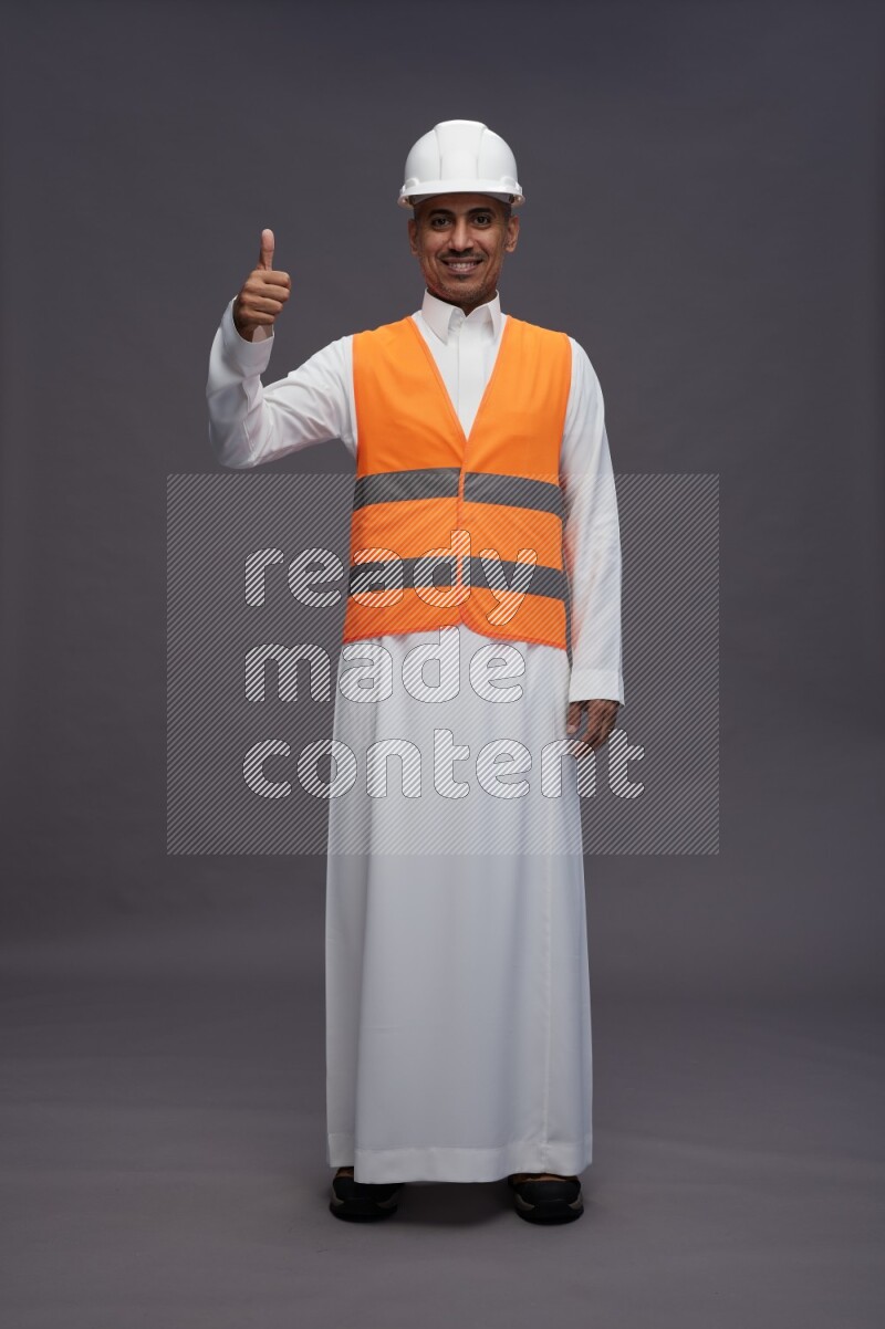 Saudi man wearing thob with engineer vest standing interacting with the camera on gray background
