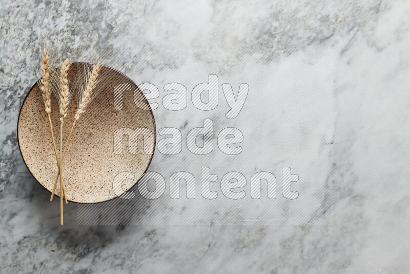 Wheat stalks on multicolored pottery plate on grey marble background