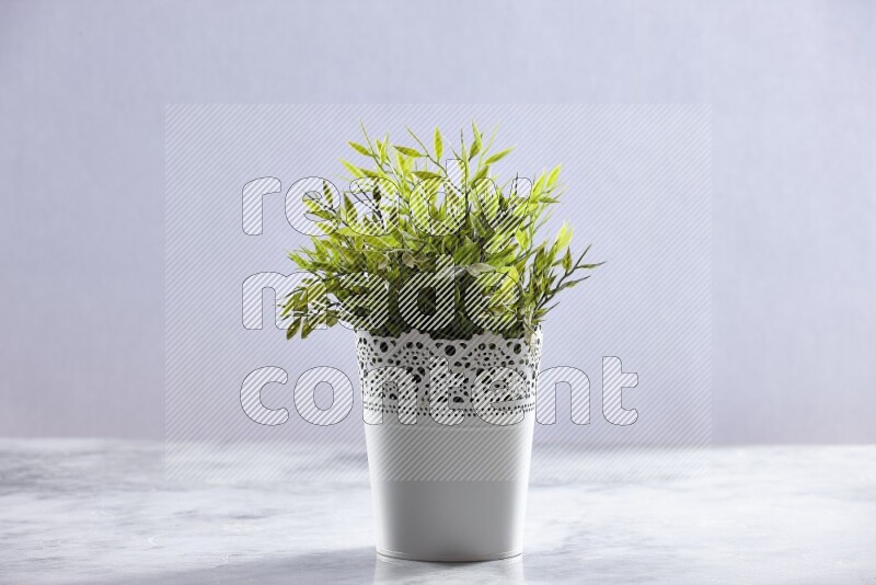 Green artificial plant in white decorative pot on grey marble background