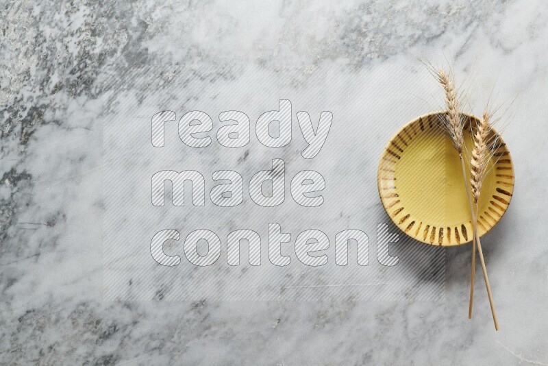 Wheat stalks on multicolored pottery plate on grey marble background