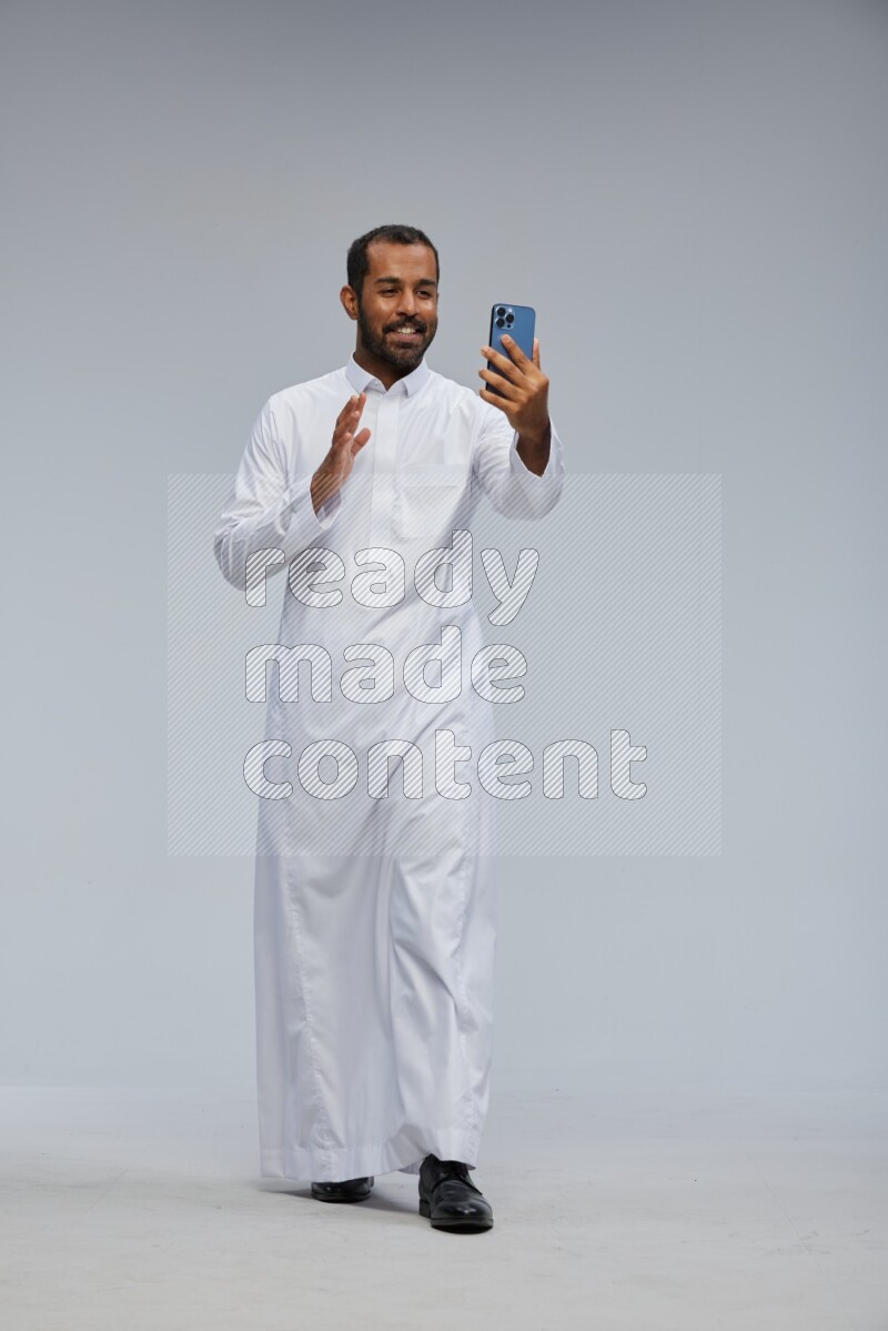 Saudi man wearing Thob standing taking selfie on Gray background