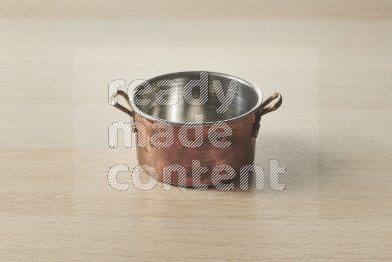 A small copper pot on light wooden background