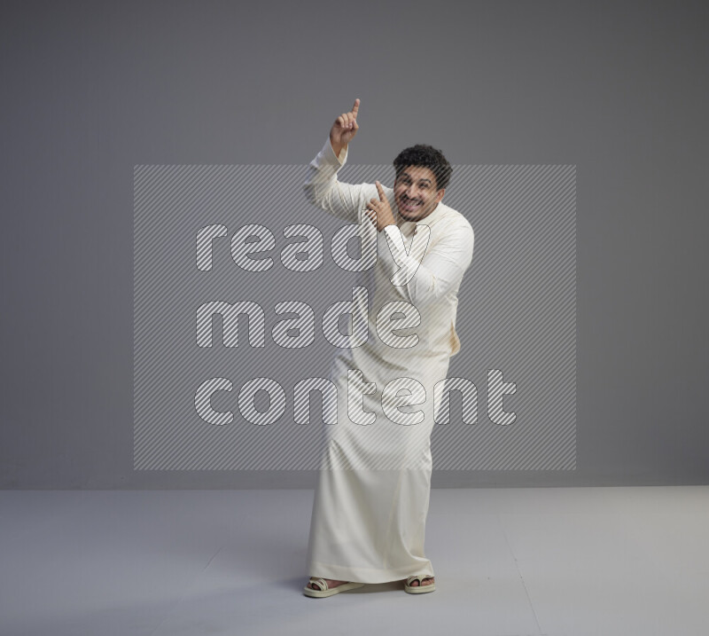 A Saudi man standing wearing thob interacting with the camera on gray background