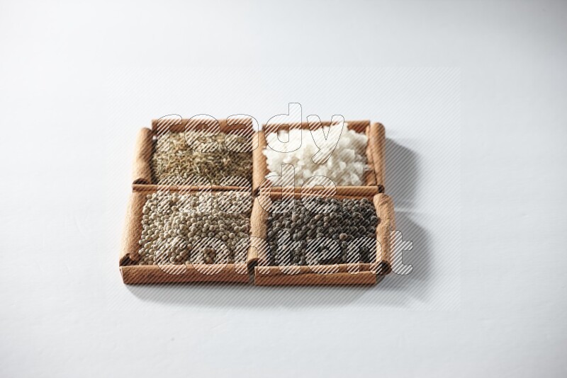 4 مربعات من أعواد القرفة ممتلئة بالكمون والملح والفلفل الأبيض والفلفل الأسود على أرضية بيضاء