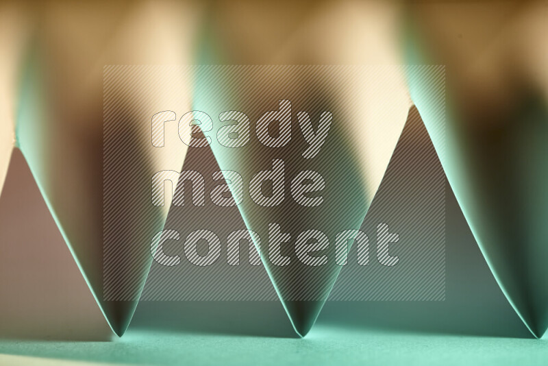 A close-up abstract image showing sharp geometric paper folds in green gradients and warm tones