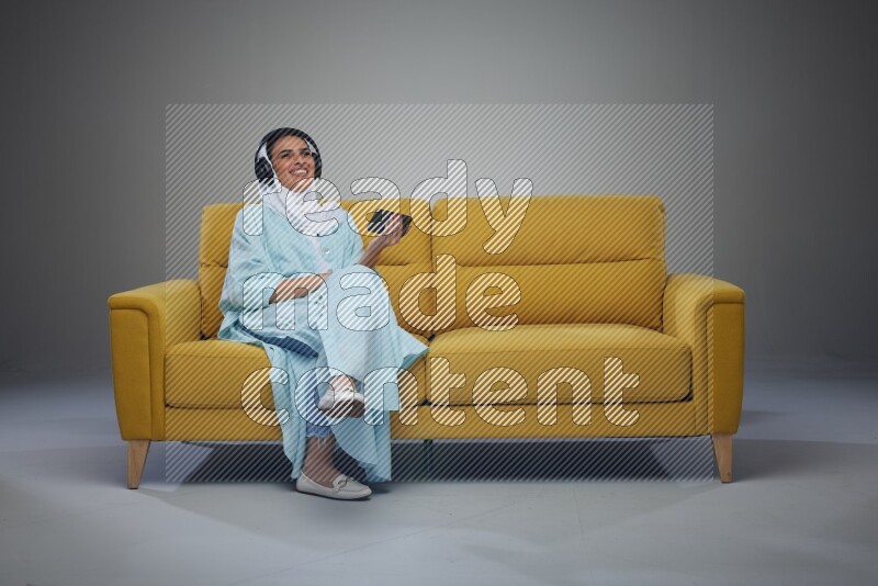 A Saudi woman sitting on a yellow Sofa Watching a Movie wearing Blue Abaya