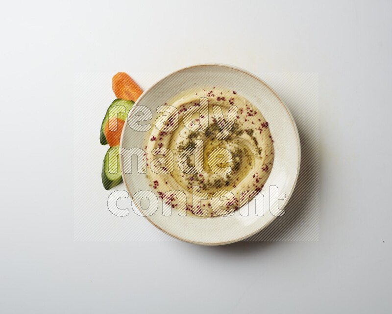 Hummus in a pottry plate garnished with zaatr & sumak on a white background