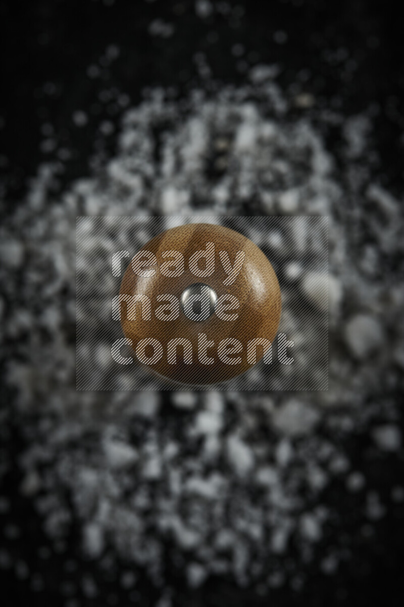A wooden grinder standing upright and surrounded by coarse white sea salt on black background