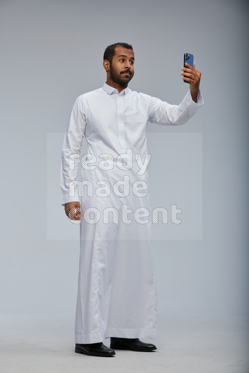Saudi man wearing Thob standing taking selfie on Gray background