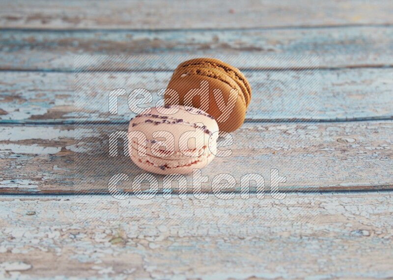 45º Shot of of two assorted Brown Irish Cream, and pink orange blossom  macarons on light blue background