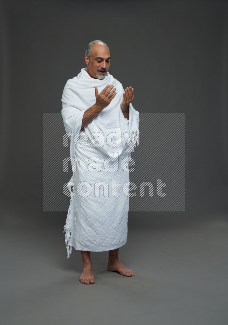 A man wearing Ehram Standing dua'a on gray background