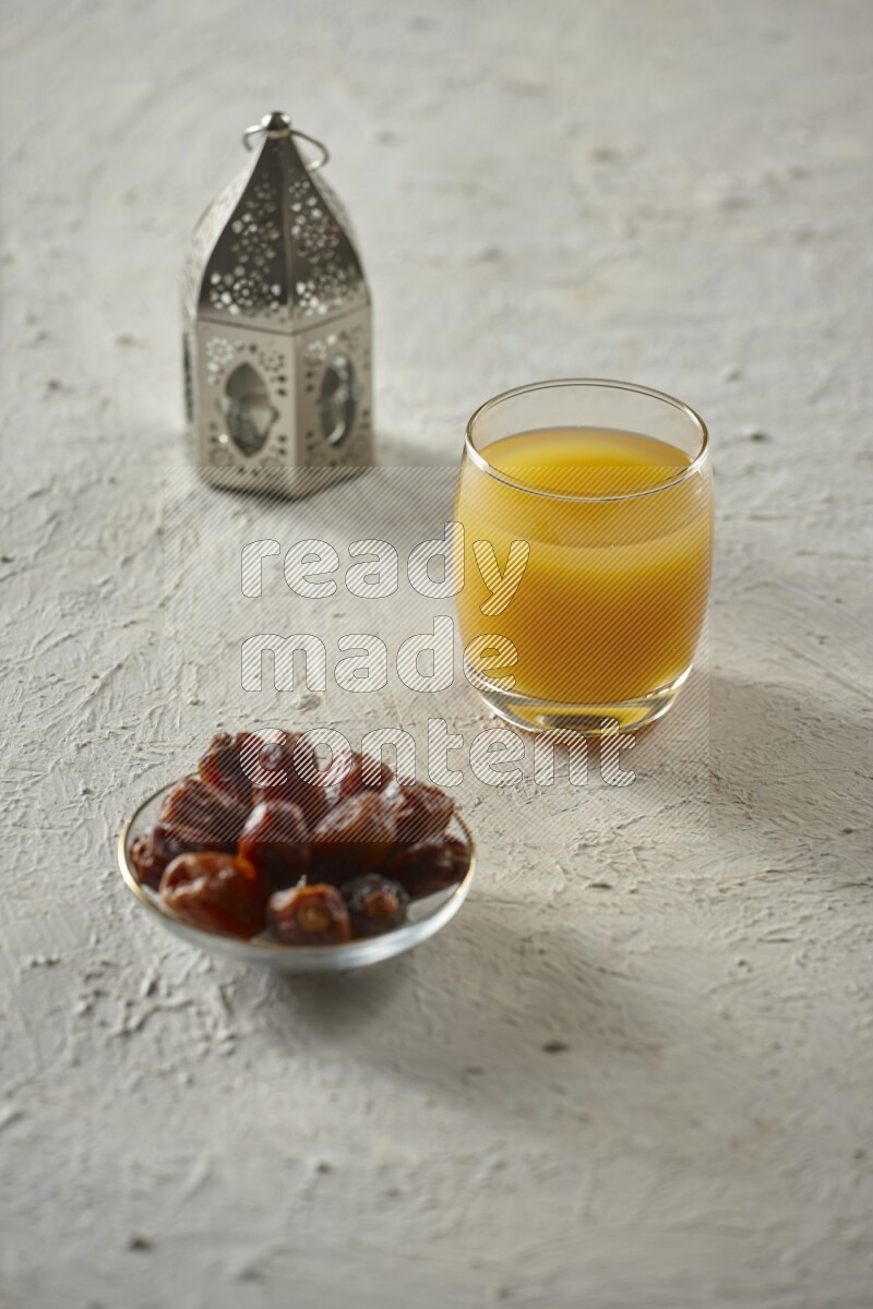 A silver lantern with different drinks, dates, nuts, prayer beads and quran on textured white background