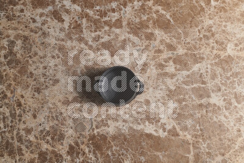 A black pottery bowl on beige marble background