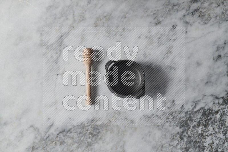 Black pottery bowl with wooden honey dipper on the side on grey marble background