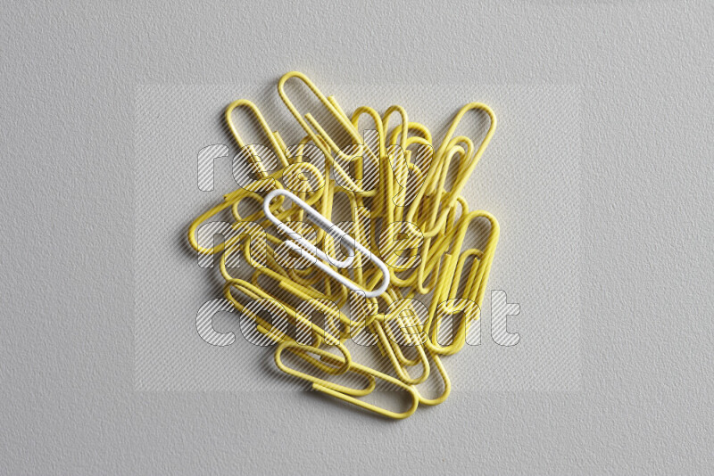 A bunch of yellow paper clips with a different colored paper clip in the center on grey background