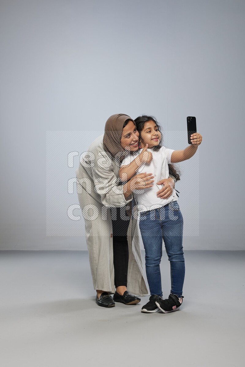 A girl standing taking selfie with her mother on gray background