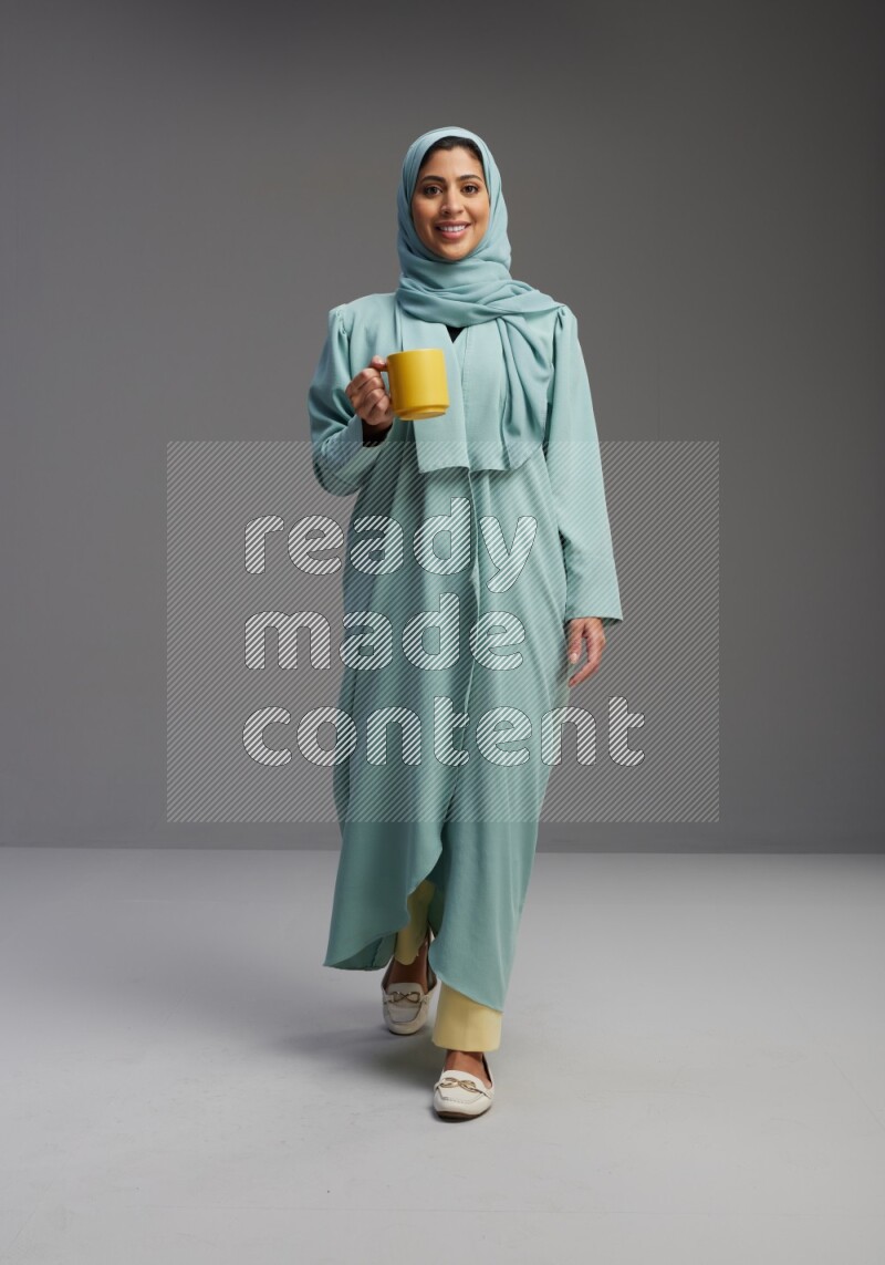 Saudi Woman wearing Abaya standing  holding a mug on Gray background