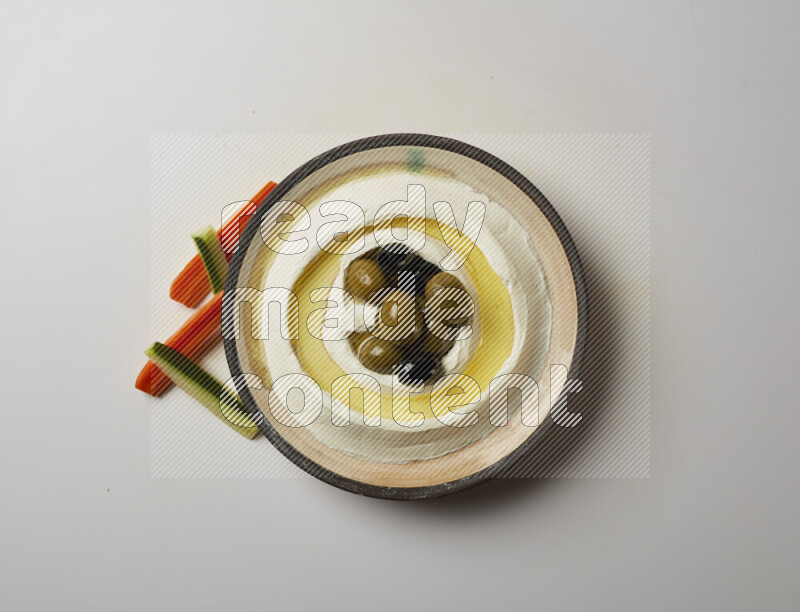 Lebnah garnished with whole black olives in a pottery plate on a white background