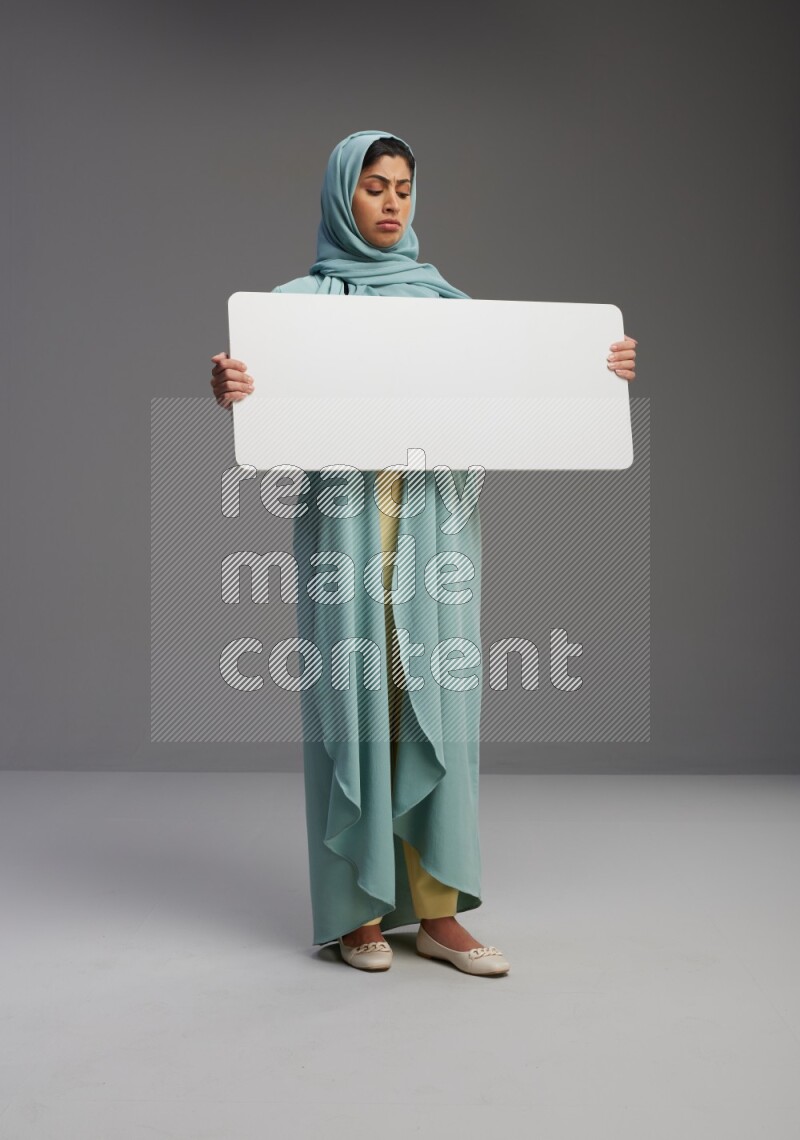 Saudi Woman wearing Abaya standing holding board on Gray background
