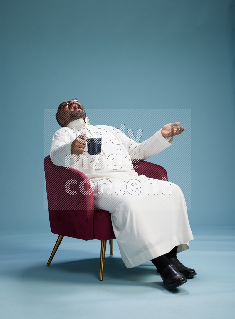 Saudi Man without shimag sitting on chair drinking coffee on blue background