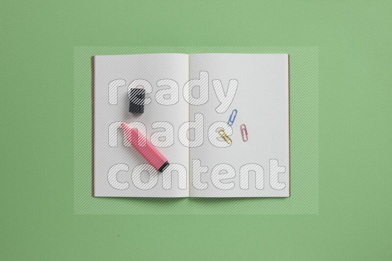 A blank open notebook with different school supplies on green background