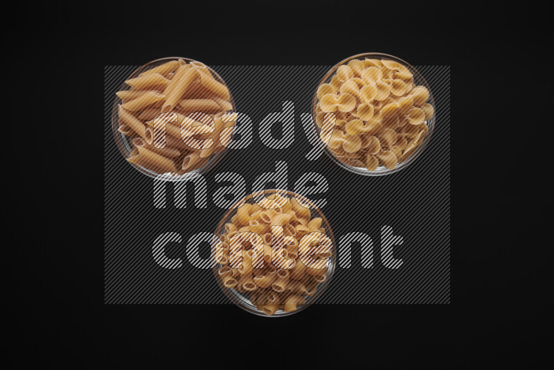 Different pasta types in glass bowls on black background