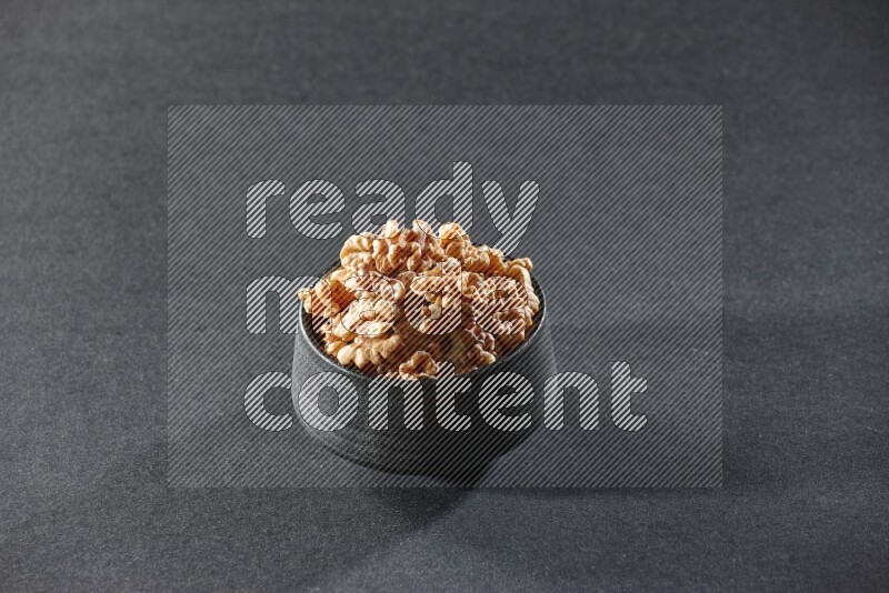 A black pottery bowl full of peeled walnuts on a black background in different angles