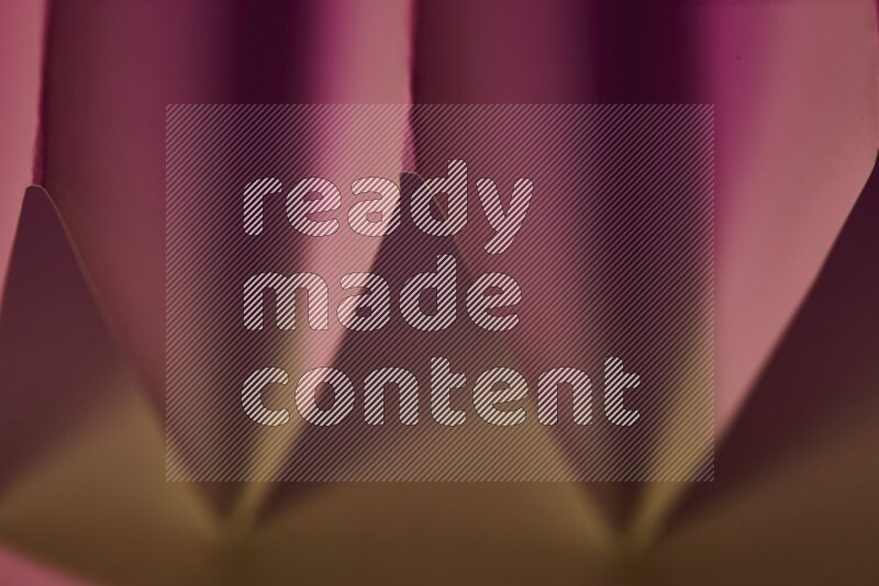 صورة مجردة مقربة تظهر طيات ورقية هندسية حادة بتدرجات اللون الوردي مع درجات لونية دافئة