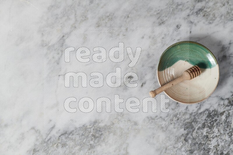 طبق فخاري متعدد الألوان مع ملعقة عسل خشبية بداخله على خلفية من الرخام الرمادي