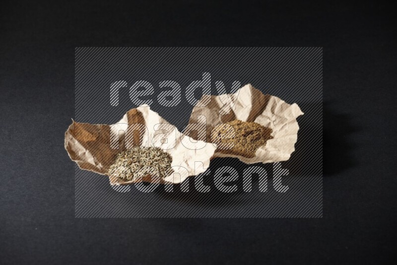 Cumin seeds and powder in 2 crumpled pieces of paper on black flooring