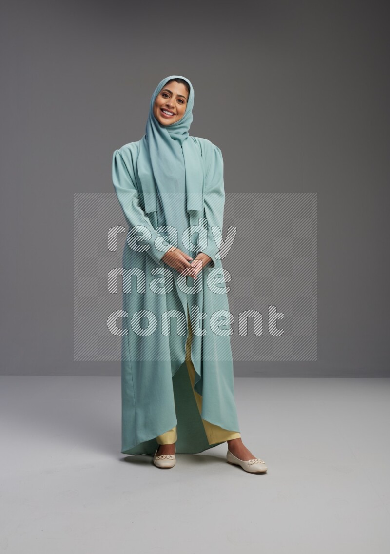 Saudi Woman wearing Abaya standing interacting with the camera on Gray background