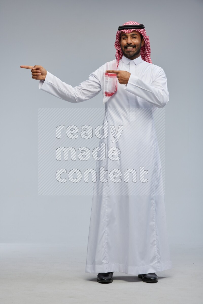 Saudi man Wearing Thob and shomag standing interacting with the camera on Gray background