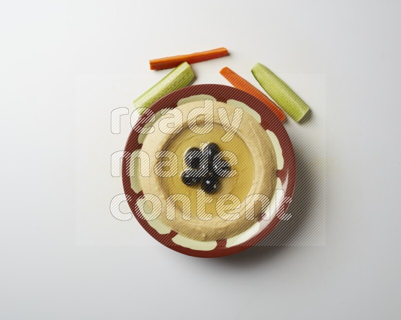 Hummus in a traditional plate garnished with black olives on a white background