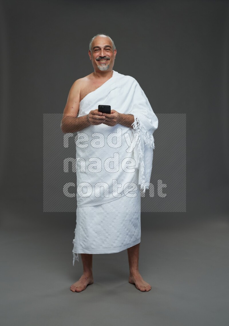 A man wearing Ehram Standing texting on phone on gray background