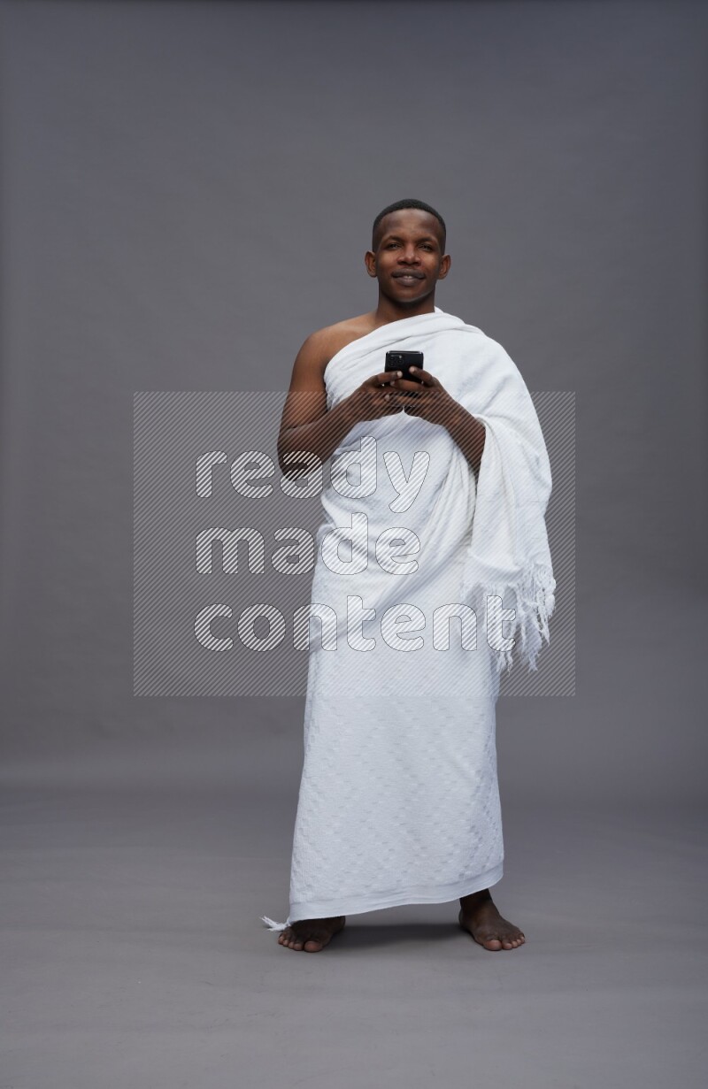A man wearing Ehram Standing texting on phone on gray background