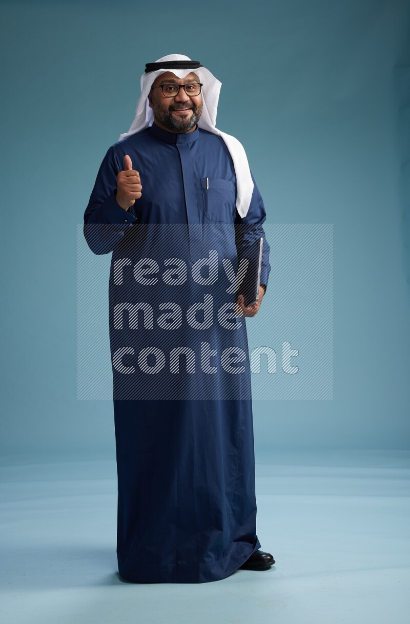 Saudi Man with shimag Standing working on laptop on blue background