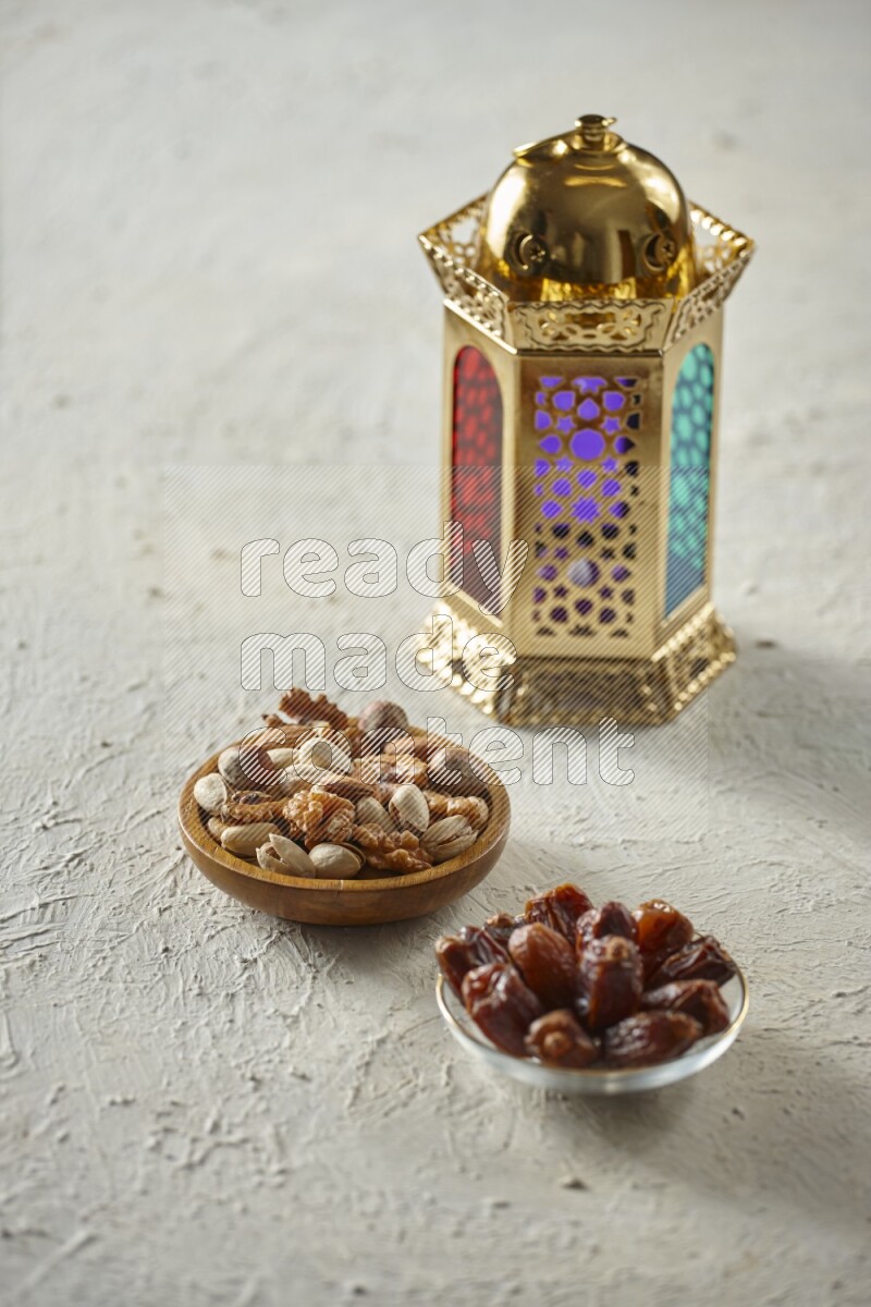 A golden lantern with different drinks, dates, nuts, prayer beads and quran on textured white background