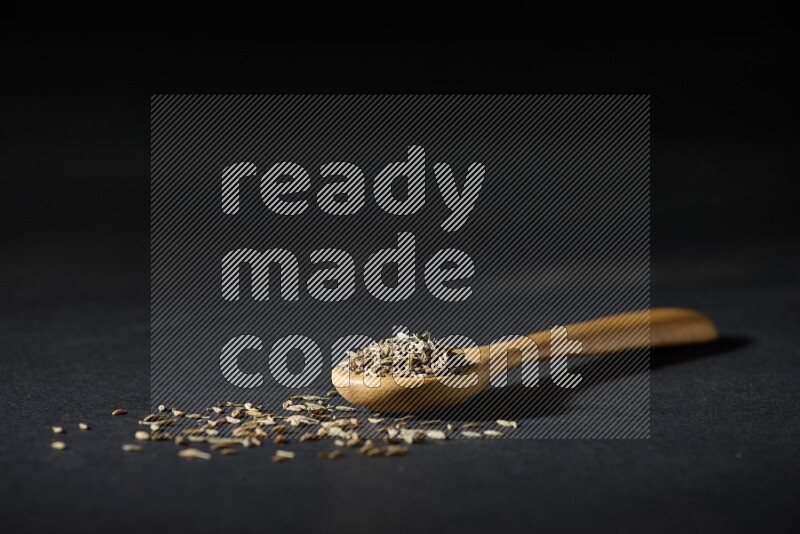A wooden spoon full of cumin seeds on black flooring