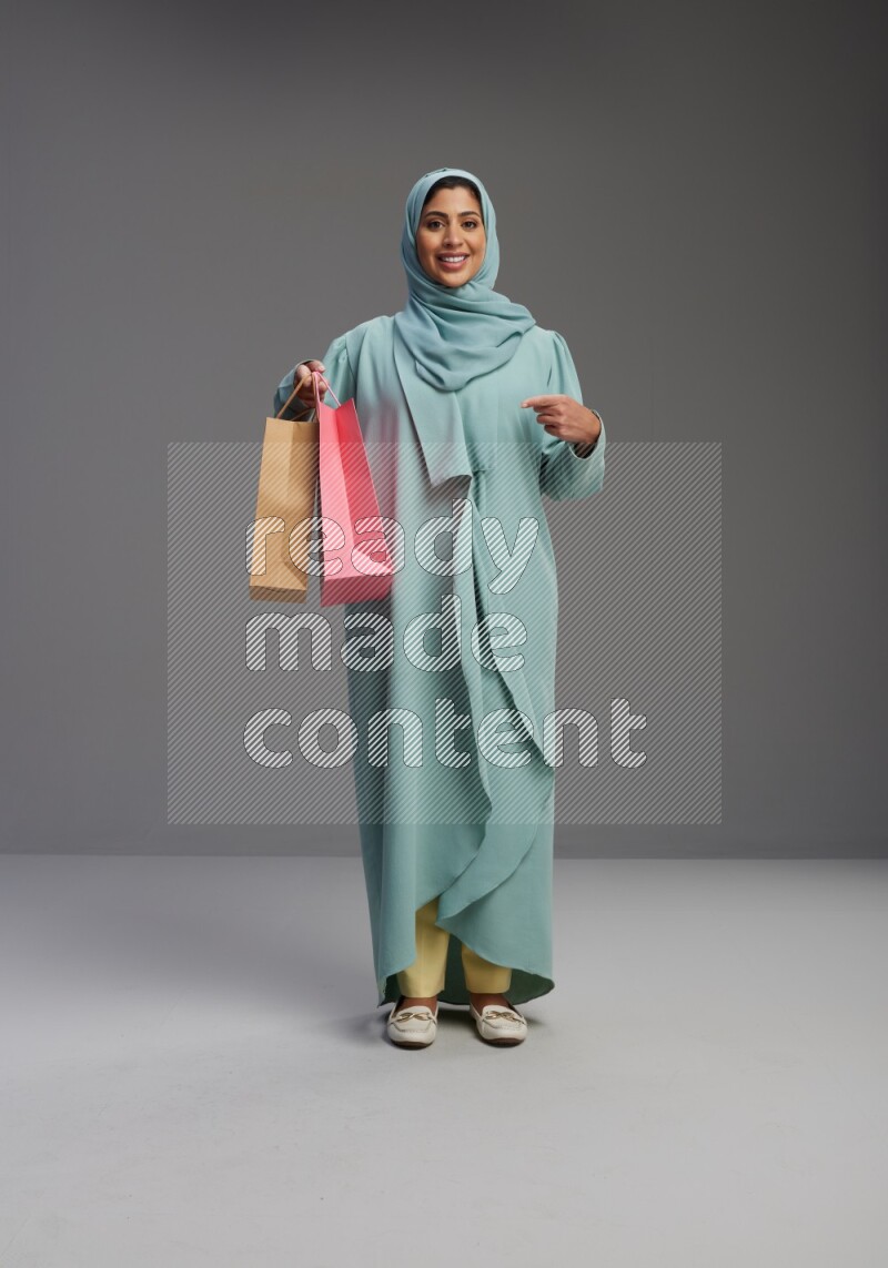 Saudi Woman wearing Abaya standing holding shopping bag on Gray background